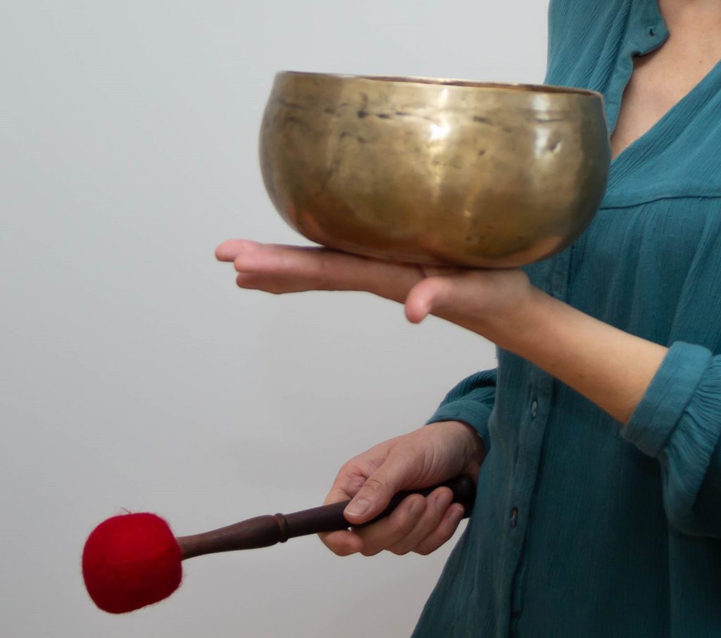 Émilie tient un bol tibétain dans la main gauche et une mailloche rouge de l'autre main